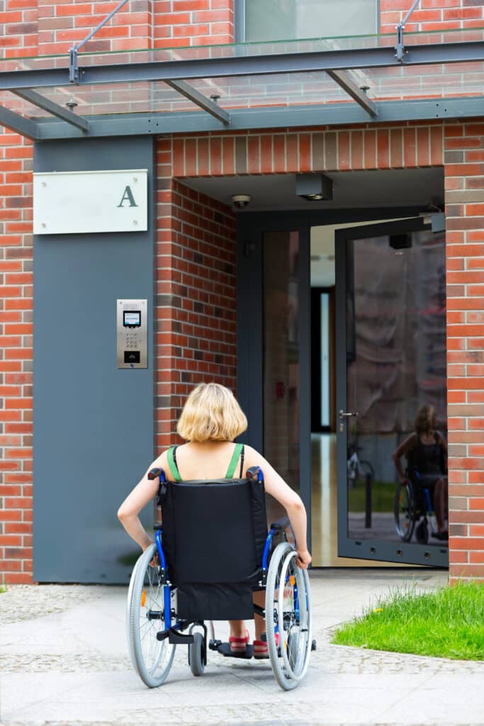 personne en fauteuil roulant avec un interphone spécial PMR en fond